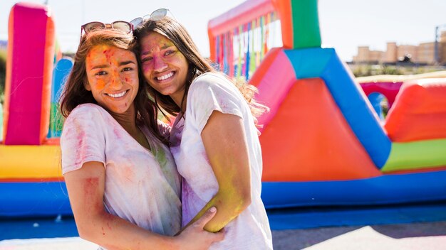 Primo piano di una giovane donna felice con colore holi sul loro abbraccio faccia