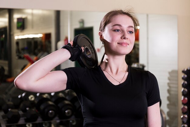 Primo piano di una giovane donna sorridente con peso in palestra