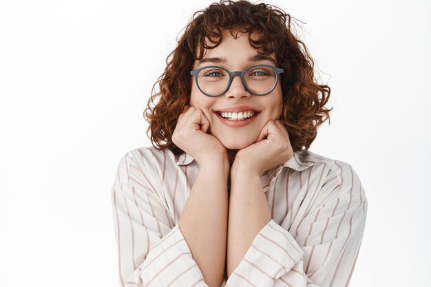 Primo piano di una giovane donna sorridente soddisfatta, guardando qualcosa di bello, fissando con ammirazione, indossando occhiali, ammirando o sognando ad occhi aperti, in piedi su sfondo bianco