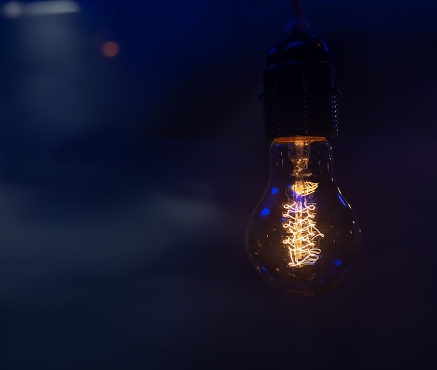 Primo piano di una lampadina incandescente appesa nello spazio scuro della copia.