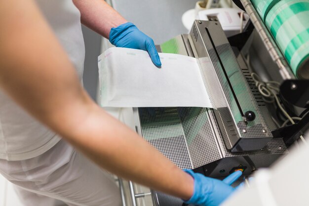 Primo piano di una mano dell&#39;infermiera facendo uso delle macchine per l&#39;imballaggio del sigillatore del sacchetto