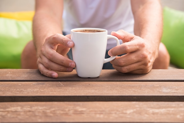 Primo piano di una mano di un uomo in possesso di una tazza di caffè con uno sfondo verde all&#39;esterno