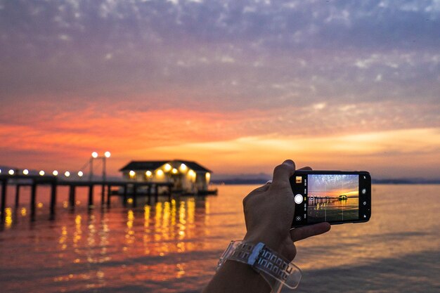 Primo piano di una mano femminile con lo smartphone che scatta foto del tramonto sul mare in Corea del Sud