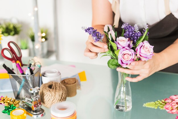 Primo piano di una mano femminile del fiorista che sistema i fiori in vaso sullo scrittorio di vetro