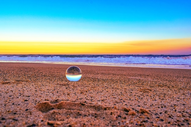 Primo piano di una palla trasparente sulla sabbia circondata dal mare durante il tramonto la sera