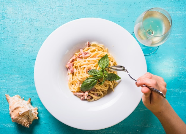 Primo piano di una persona che mangia gli spaghetti con carne e basilico foglia sul piatto