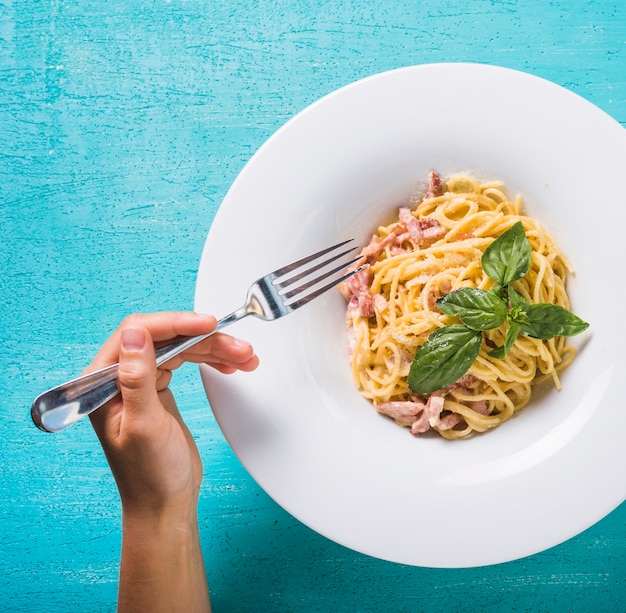 Primo piano di una persona che mangia gli spaghetti con la forcella sul fondo del turchese