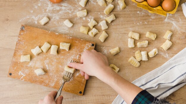 Primo piano di una persona che preme la pasta con la forchetta sul tagliere