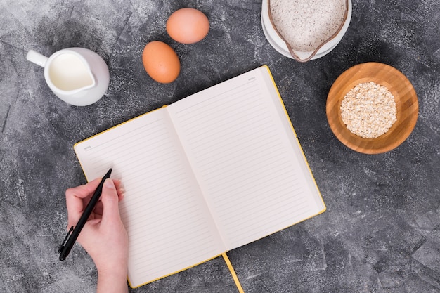 Primo piano di una persona che scrive nel diario con gli ingredienti del pane sul contesto concreto