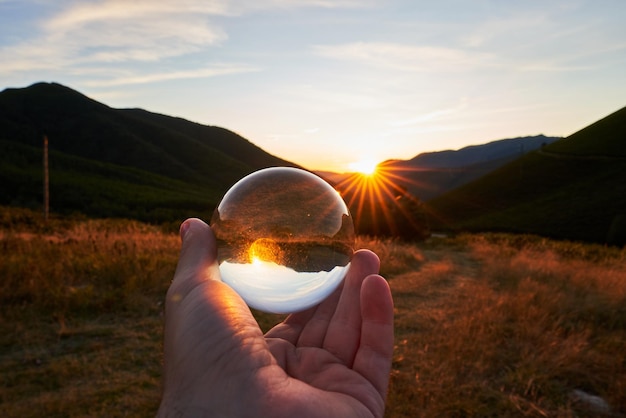 Primo piano di una persona che tiene una sfera di cristallo con l'ambiente che si riflette su di essa sotto la luce del sole