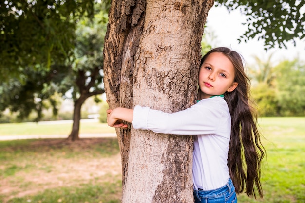 Primo piano di una ragazza adorabile che abbraccia il tronco d&#39;albero