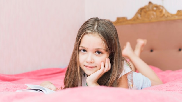 Primo piano di una ragazza che si trova sul libro di lettura del letto rosa