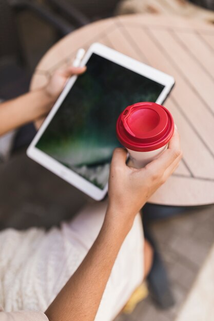 Primo piano di una ragazza che tiene compressa digitale e tazza di caffè a gettare