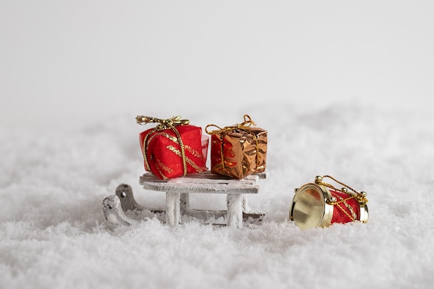 Primo piano di una slitta e contenitori di regalo colorati nella neve, giocattoli di Natale nei precedenti bianchi