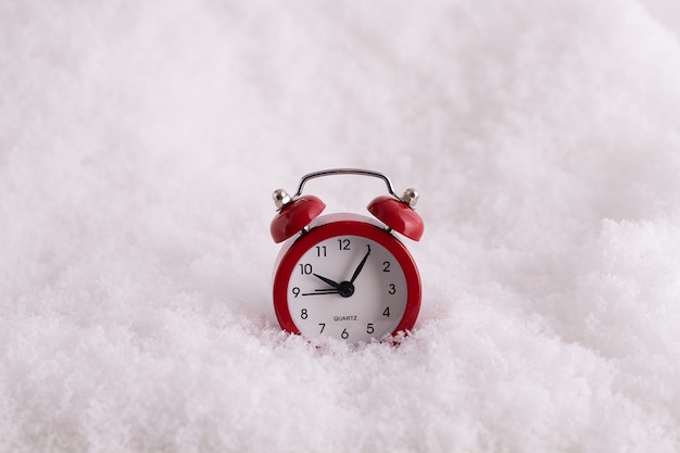 Primo piano di una sveglia rossa nella neve, un orologio che conta il tempo fino al nuovo anno