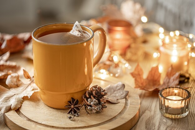 Primo piano di una tazza di tè tra le foglie autunnali e le candele su uno sfondo sfocato.