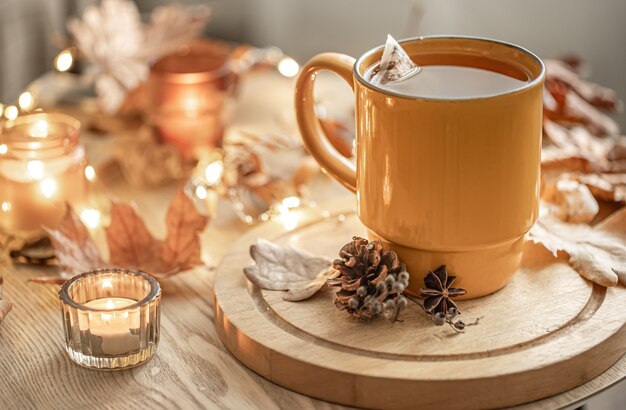 Primo piano di una tazza di tè tra le foglie autunnali e le candele su uno sfondo sfocato.