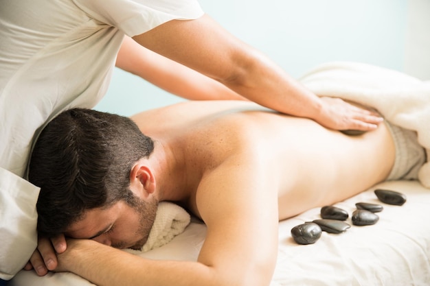 Primo piano di una terapista femminile che fa un massaggio con pietre calde a un giovane in una stazione termale