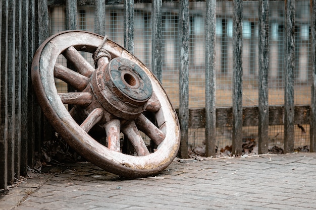 Primo piano di una vecchia ruota di legno a terra contro le recinzioni sotto le luci