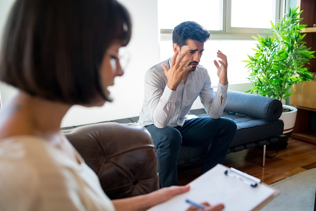 Primo piano di uno psicologo che prende appunti negli appunti durante la sessione di terapia con il suo paziente preoccupato. Psicologia e concetto di salute mentale.