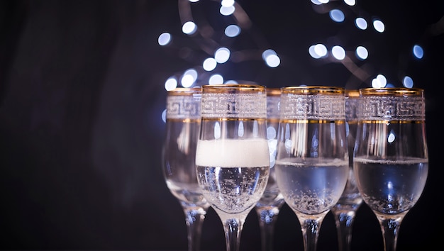 Primo piano di vetro trasparente con champagne contro il fondo scuro del bokeh