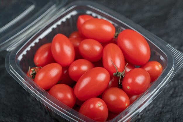 Primo piano foto di piccoli pomodori rossi in un contenitore di plastica. Foto di alta qualità