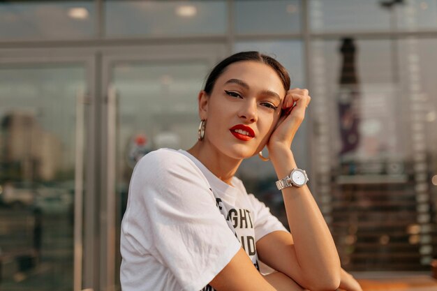 Primo piano ritratto all'aperto di adorabile affascinante bruna con labbra rosse in posa davanti alla macchina fotografica in città Bella signora carina che riposa all'aperto