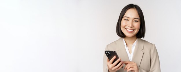 Primo piano ritratto di donna coreana donna aziendale in tuta utilizzando il telefono cellulare e sorridente tenendo smar