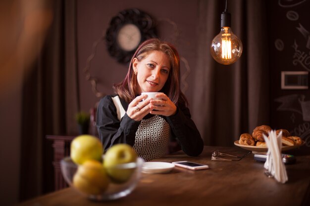 Primo piano ritratto di donna d'affari adulta che sorride mentre tiene in mano una tazza di caffè. Rilassarsi in una caffetteria vintage