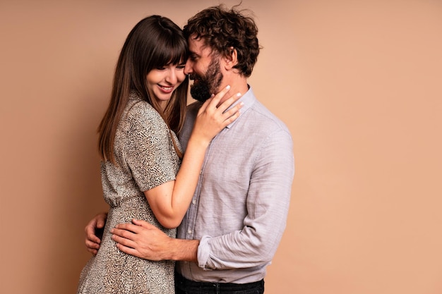 Primo piano ritratto in studio di coppia di mezza età innamorata, baci e abbracci, felici insieme, abiti da sera glamour, pronti per la celebrazione, sfondo beige.