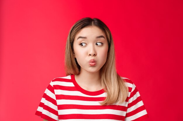 Primo piano sciocco tenera giovane ragazza asiatica moderna taglio di capelli biondo trattenere il respiro piegando le labbra e imbronciato sguardo...