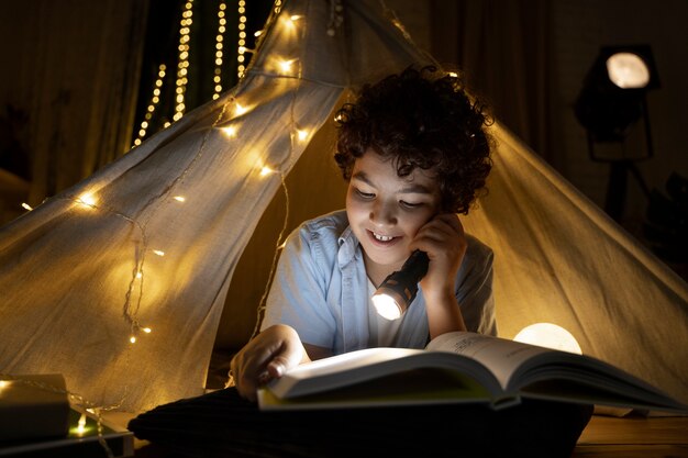 Primo piano sul bambino che legge nella sua tenda di casa