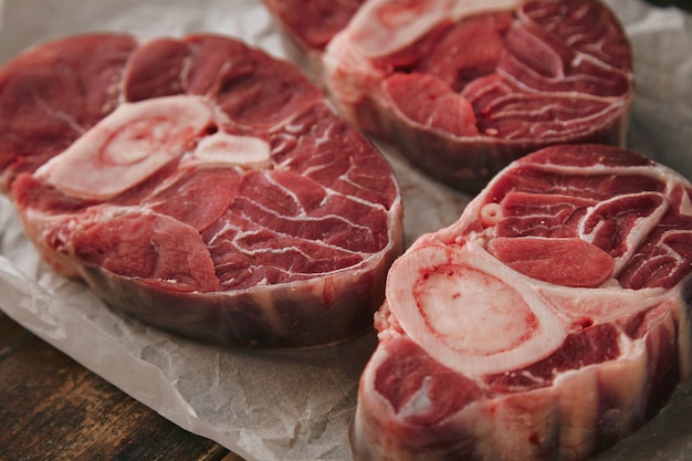 Primo piano tre bistecche di carne cruda fresca con osso su carta artigianale bianca dall'alto