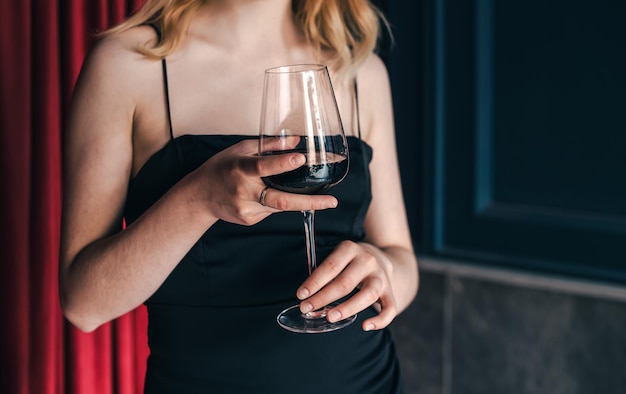Primo piano un bicchiere di vino nelle mani di una donna in un abito da sera