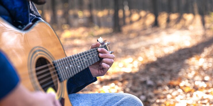 Foto gratuito primo piano un uomo suona una chitarra acustica nella foresta autunnale