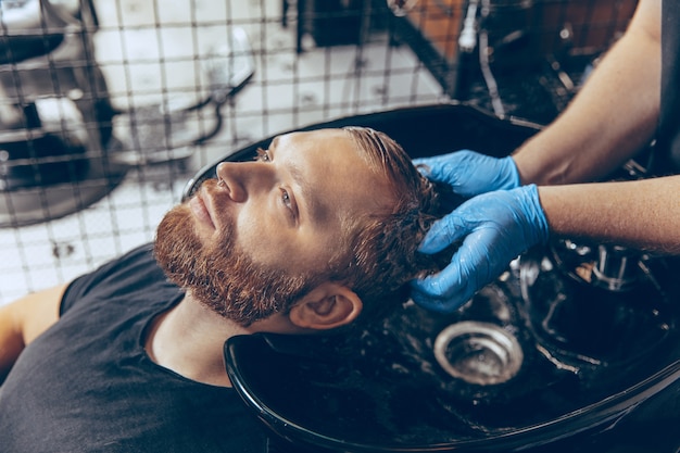 Primo piano uomo che si taglia i capelli dal barbiere che indossa la maschera durante la pandemia di coronavirus.