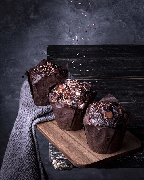 Primo piano verticale di tre deliziosi muffin al cioccolato su sfondo grigio scuro