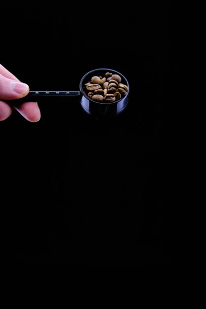 Primo piano verticale di una persona che tiene un cucchiaio con i chicchi di caffè isolati sul nero