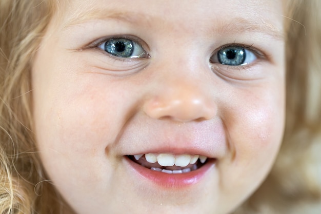 Primo piano volto di una bambina carina con grandi occhi azzurri, ragazza sorridente.