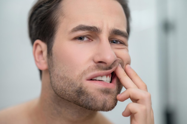 Problemi dentali. Uomo che si controlla i denti e sembra turbato