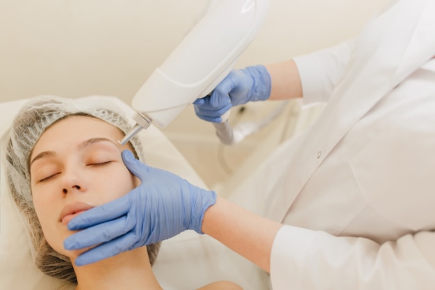 Procedure di cosmetologia, ringiovanimento di una donna abbastanza giovane nel salone di bellezza. Procedura di dermatologia, mani in bagliori blu, al lavoro, assistenza sanitaria, terapia, botox, iniezioni