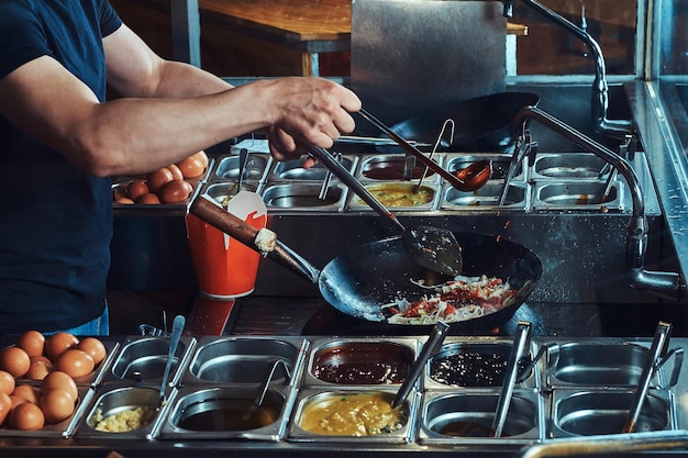 Processo di cottura in un ristorante asiatico. Cuocere è friggere le verdure con spezie e salsa in un wok