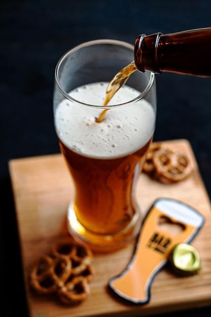 Processo di versamento della birra ambrata nel bicchiere su una tavola di legno e snack