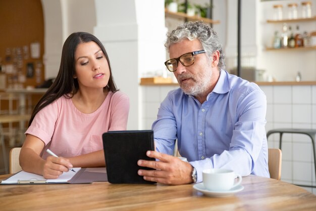 Professionista maschio maturo serio che mostra contenuto sul tablet al giovane collega