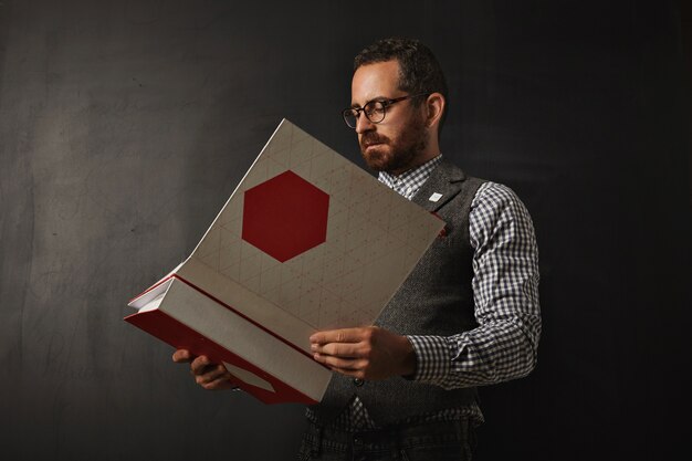 Professore barbuto serio in camicia oxford scozzese e gilet di tweed legge il nuovo piano educativo per il suo studente per il prossimo anno all'università