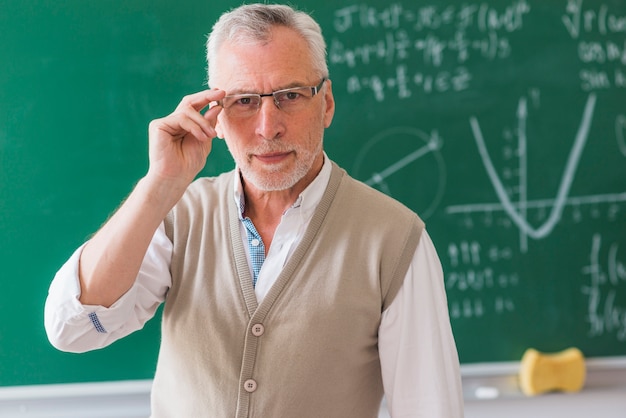 Professore senior che corregge i vetri contro la lavagna con il problema di per la matematica