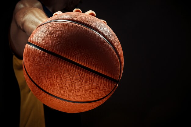 Profili il punto di vista di una palla del canestro della tenuta del giocatore di pallacanestro su fondo nero