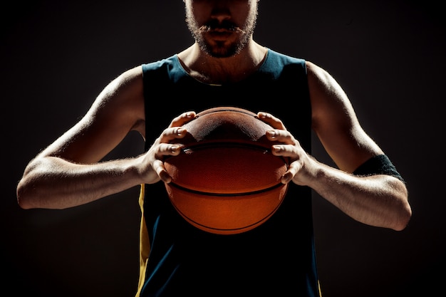 Profili il punto di vista di una palla del canestro della tenuta del giocatore di pallacanestro su spazio nero