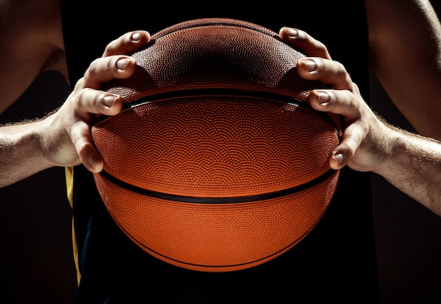 Profili il punto di vista di una palla del canestro della tenuta del giocatore di pallacanestro sulla parete nera