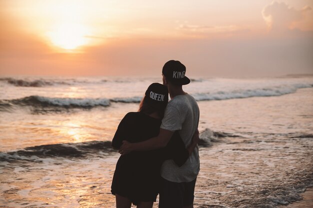 Profili il ritratto di giovani coppie romantiche che camminano sulla spiaggia. Ragazza e il suo ragazzo in posa al tramonto colorato d'oro. Si abbracciano e sognano